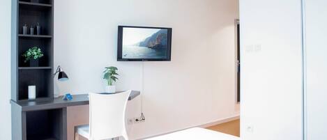 A modern room with a desk, chair, and a television mounted on the wall displaying a scenic view.