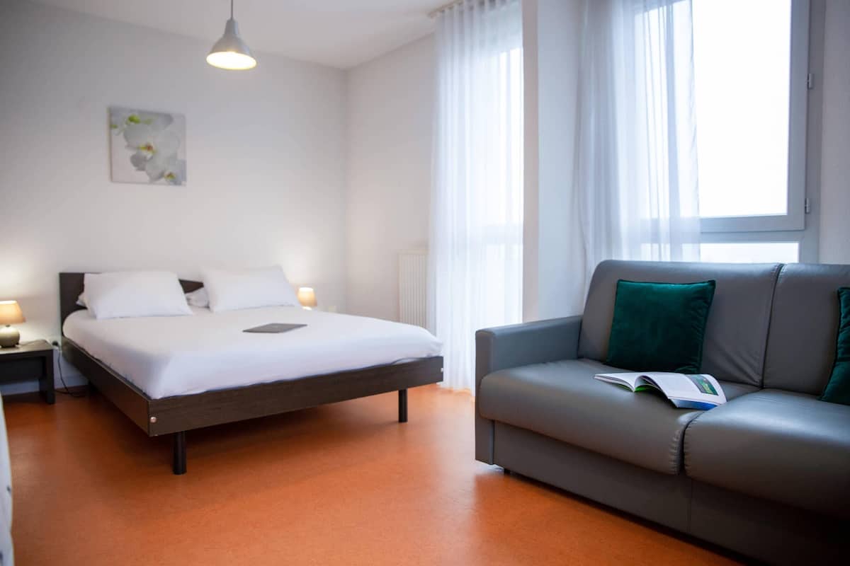 Una habitación de hotel moderna con cama, sofá y ventana con cortinas translúcidas.