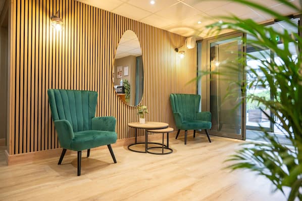 A modern waiting area with two green armchairs, a small round table, and a mirror on the wall.