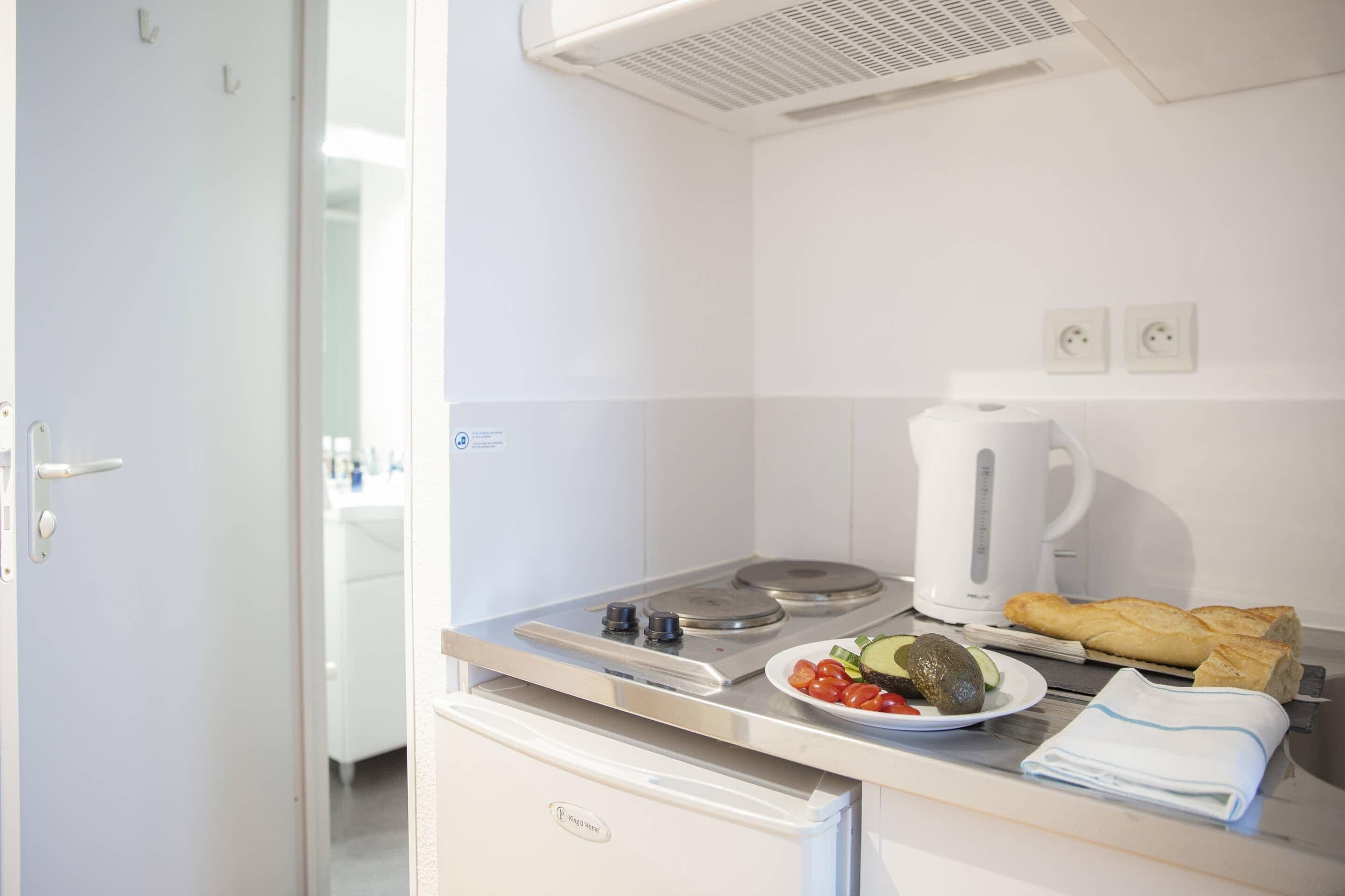 A compact kitchenette with a stove, a kettle, and a small refrigerator.