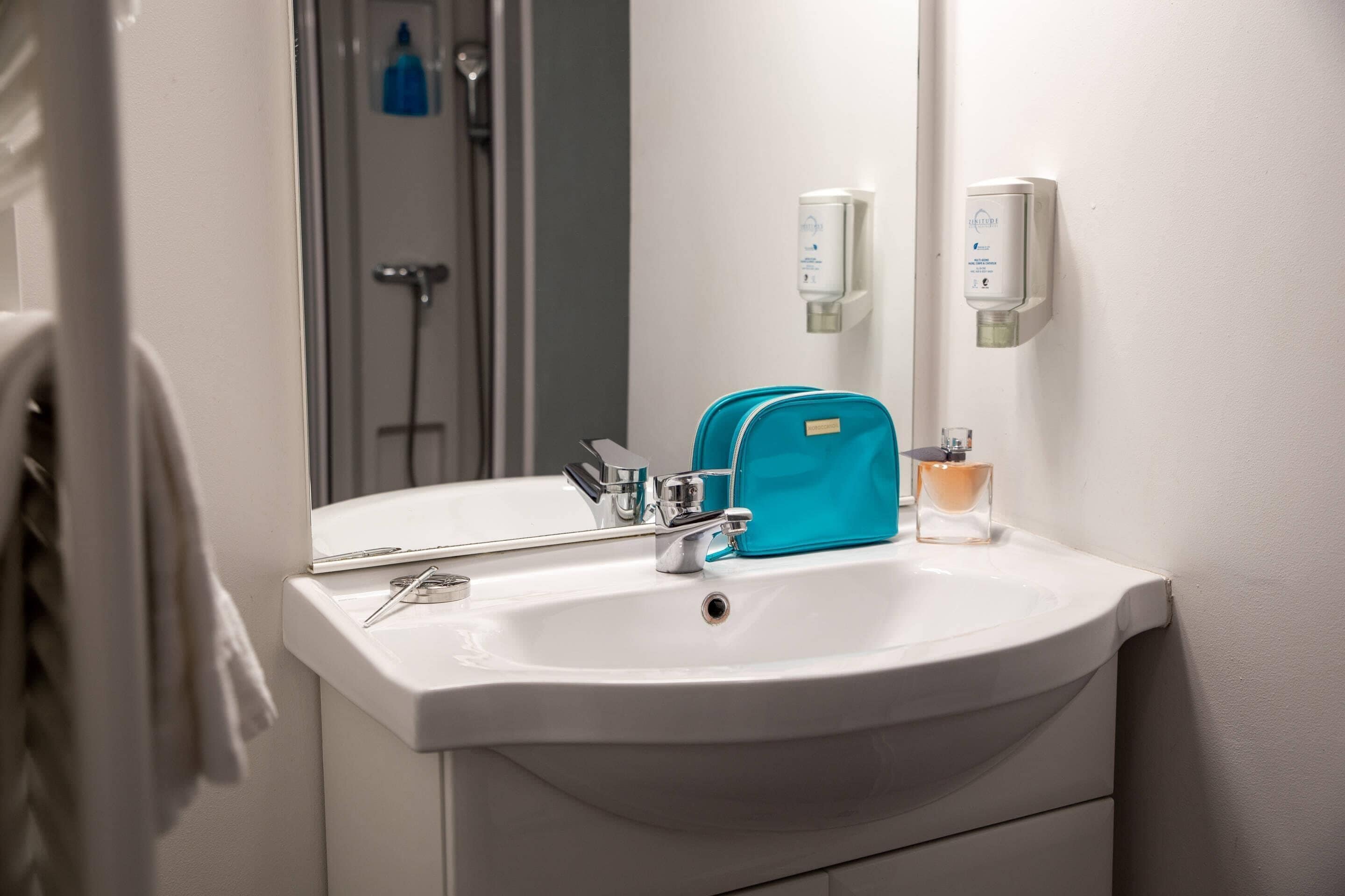 A bathroom with a white sink, a mirror, a blue toiletry bag, and two soap dispensers.