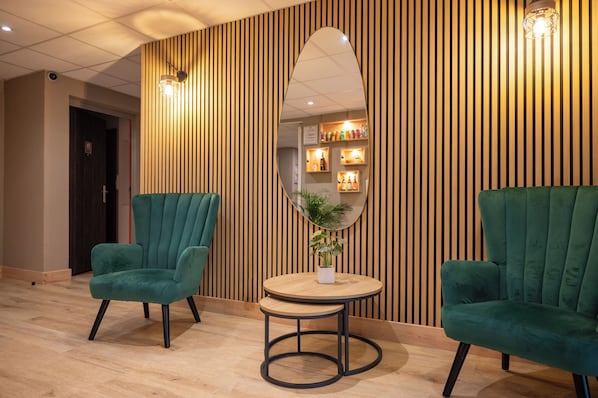 Una habitación con dos sillones verdes, una mesa redonda de madera y un espejo grande en una pared de listones de madera.