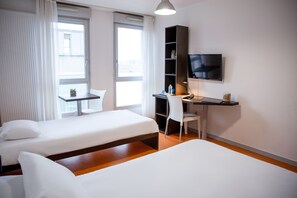 Una habitación de hotel con dos camas, un escritorio con silla, televisión y ventana con cortinas.