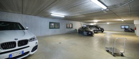 A parking garage with concrete walls, fluorescent lighting, and several parked cars including a white BMW.