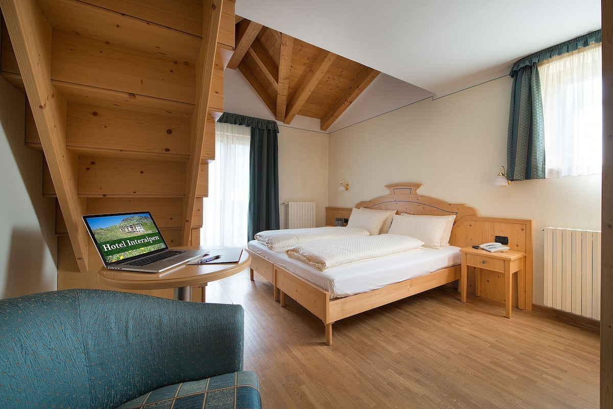 Dormitorio con estructura de madera, una cama, mesita de noche y un ordenador portátil que muestra 'Hotel Interalpen'.