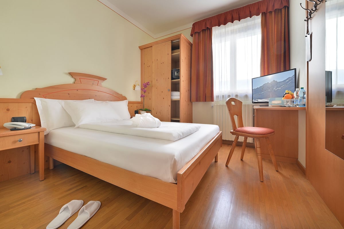 Una habitación de hotel con una cama de madera, un escritorio con una computadora, una silla y un armario.