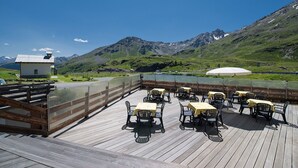 Een terras met tafels en stoelen, met uitzicht op een bergachtig landschap.