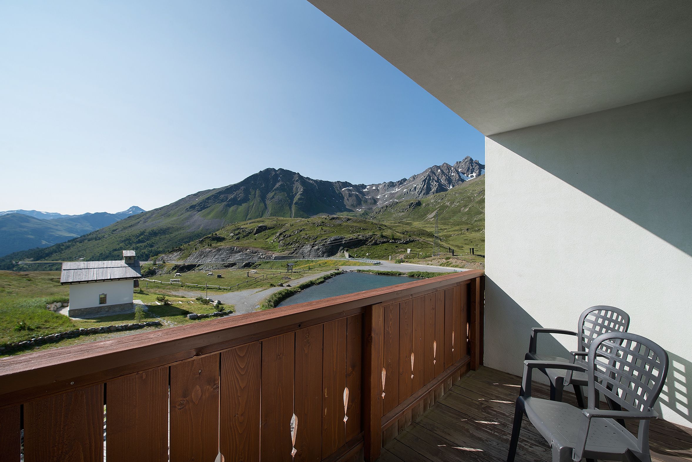 A balcony with a view of a mountain, a small house, and a body of water.