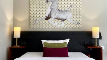 A hotel room with a bed, two bedside lamps, a headboard, and a wall-mounted artwork of a horse.