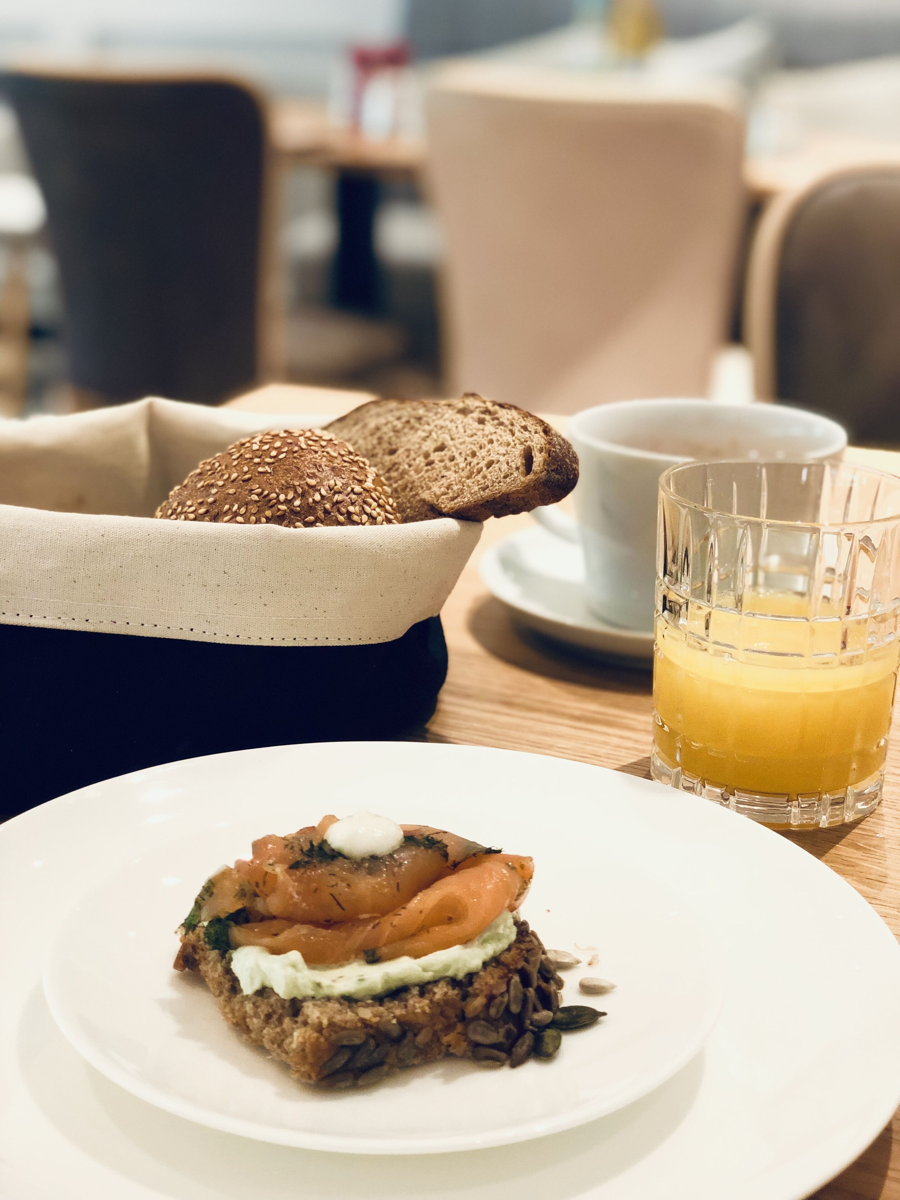 Un desayuno con un plato de comida, un bol de pan, una taza de café y un vaso de zumo de naranja.