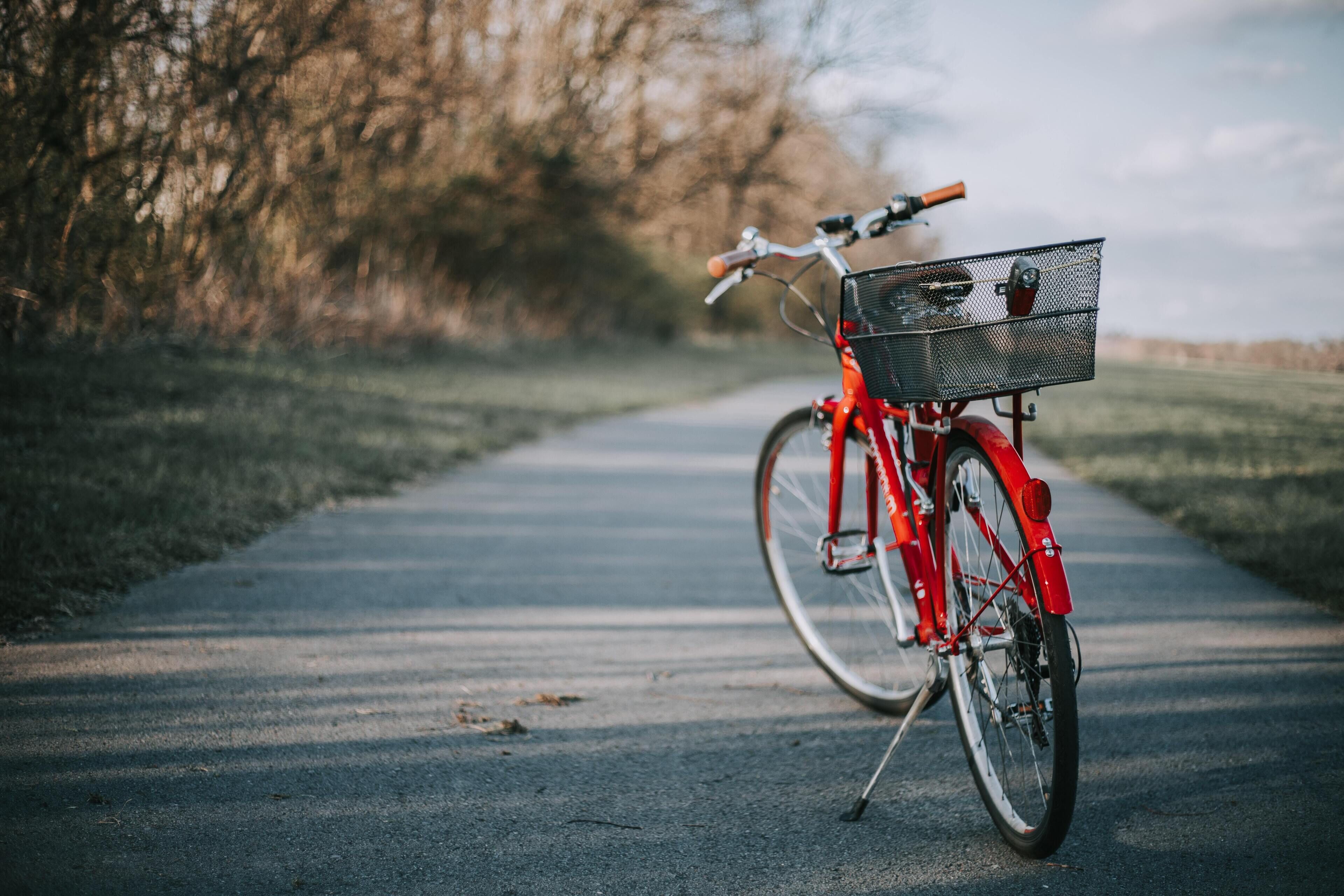 Una bicicleta roja estacionada en un sendero pavimentado con una cesta trasera.