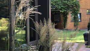A modern building with large windows, a brick pathway, and various plants including tall grasses and ferns. - Heidegrund (Garrel)