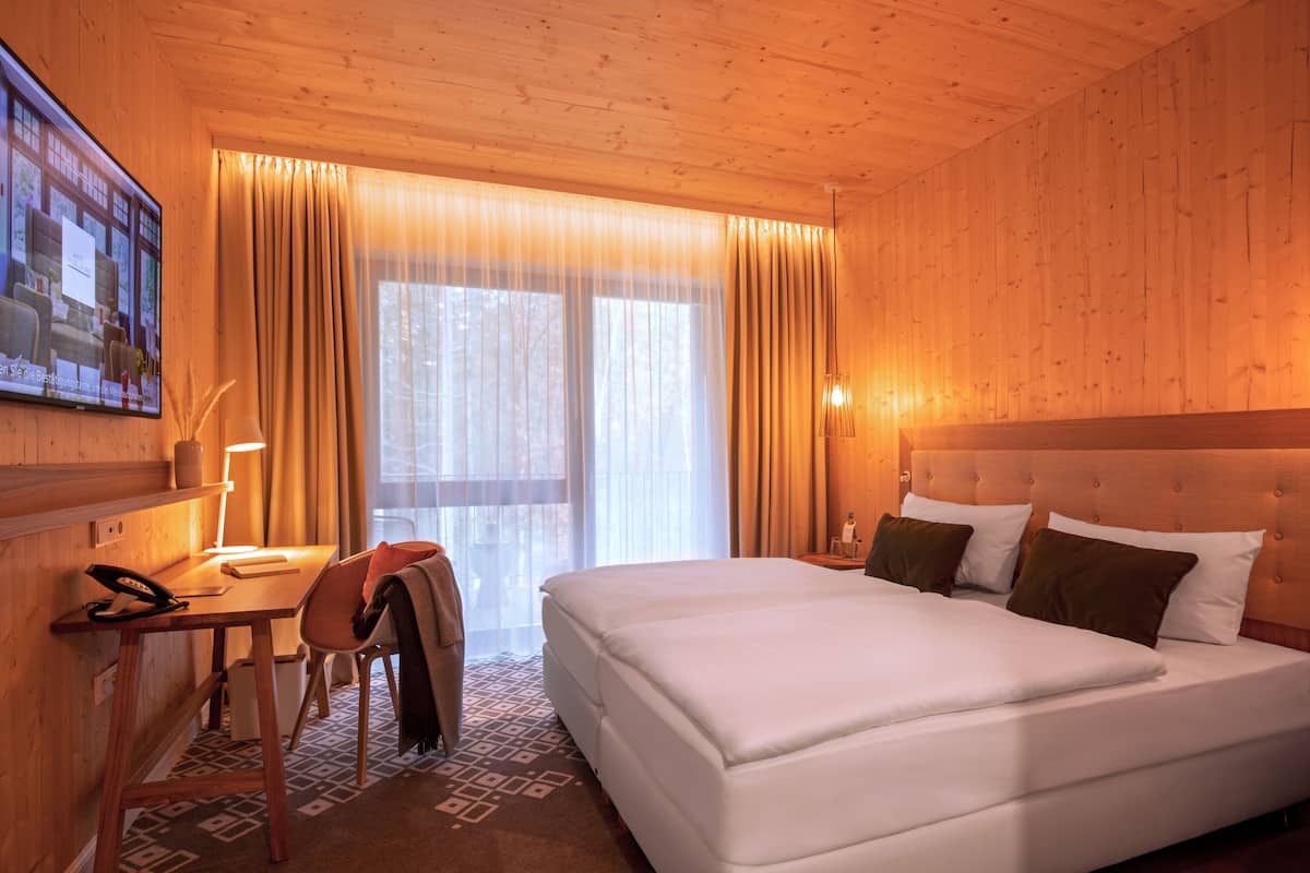 Ett hotellrum med träinredning, en säng med vita sängkläder, ett skrivbord med en lampa och en stol.