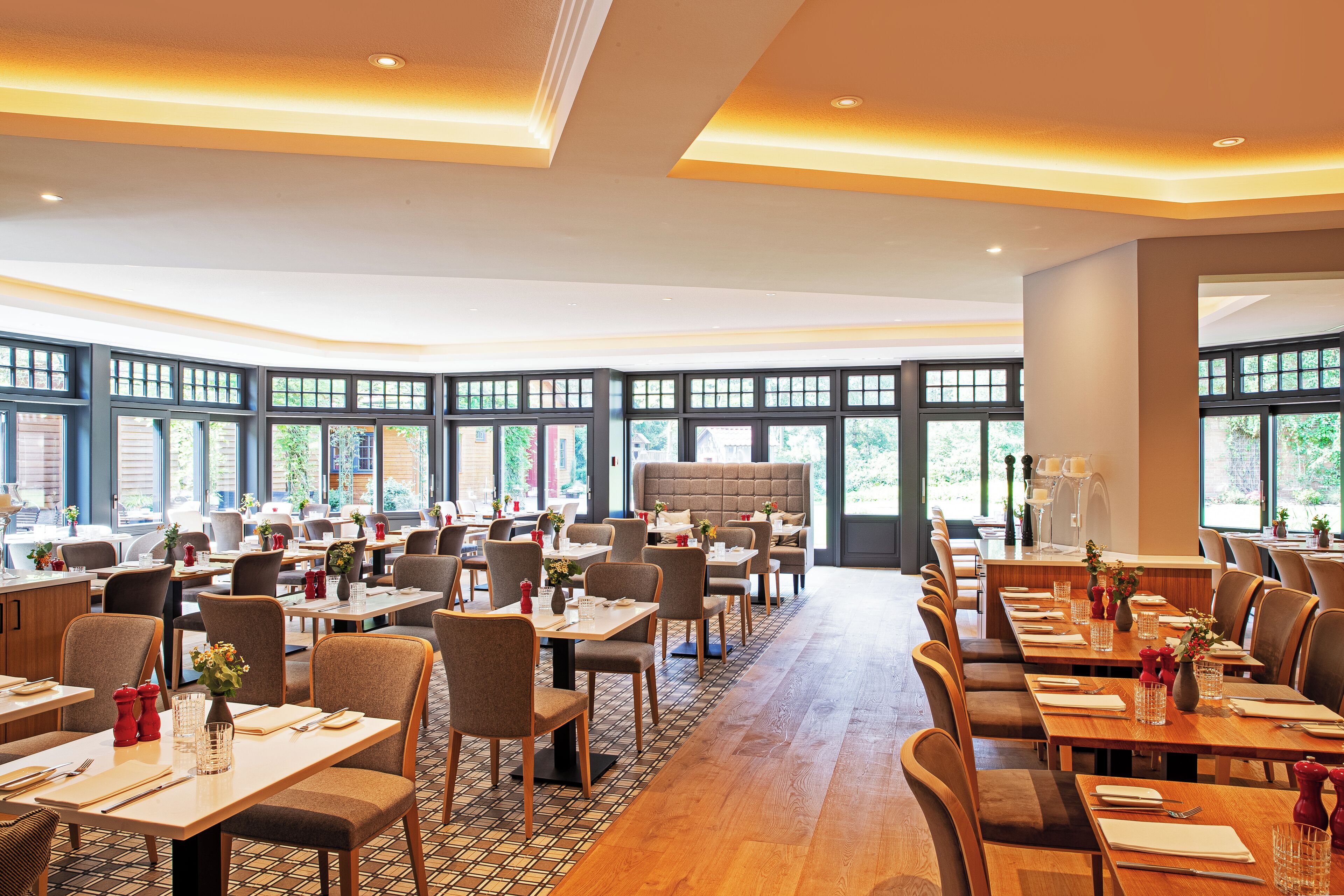 A spacious dining area with multiple tables and chairs, large windows, and a modern ceiling design.
