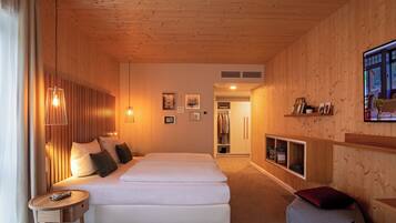Una habitación de hotel moderna con techo de madera, una cama con ropa de cama blanca, una mesita redonda pequeña y un televisor fijado a la pared.