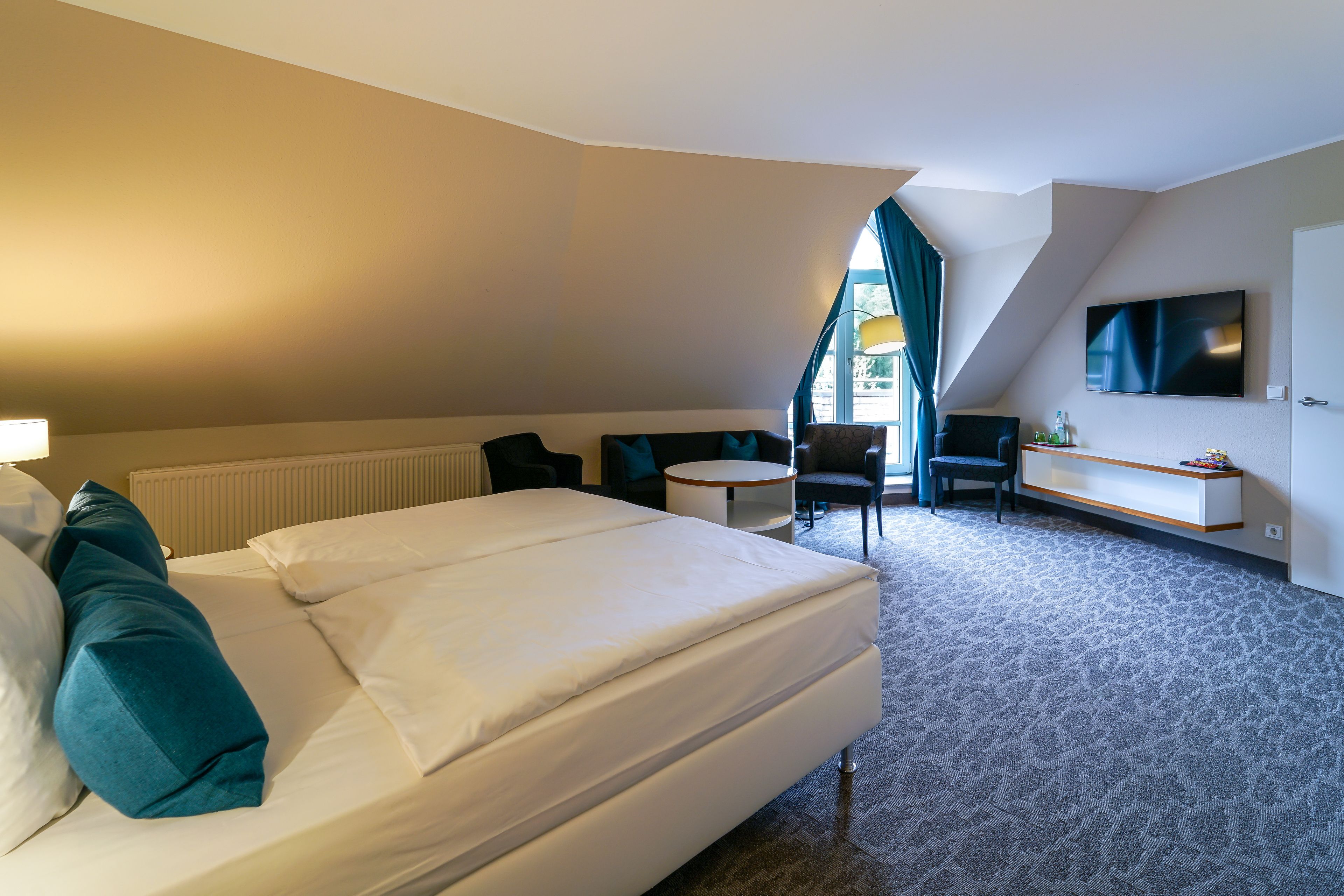 A hotel room with a large bed, a desk, a chair, and a TV on the wall.