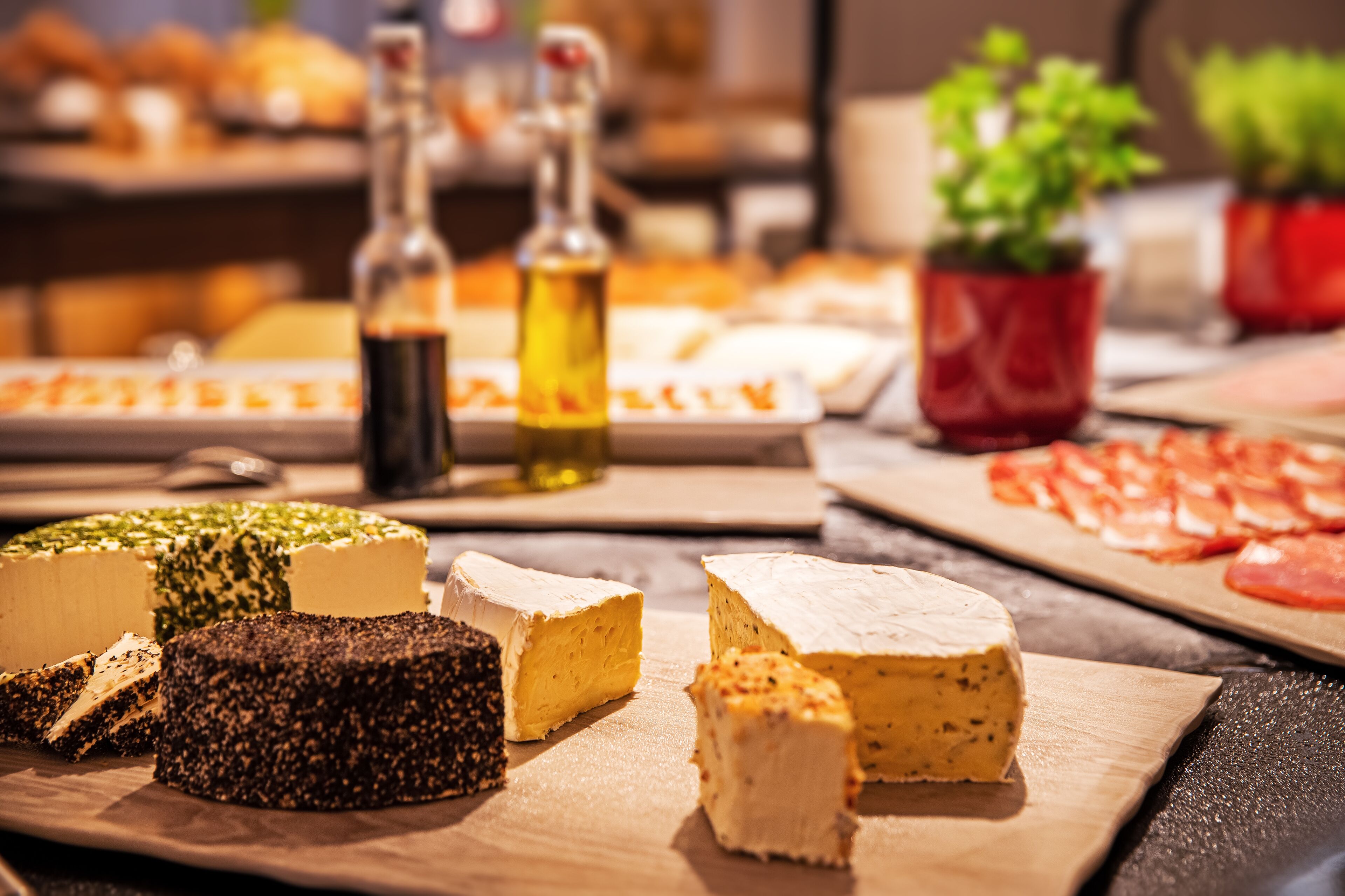 Une sélection de fromages présentés sur une planche en bois, accompagnés de bouteilles d’huile d’olive et d’une autre planche avec des tomates coupées en tranches.