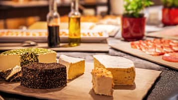Une sélection de fromages présentés sur une planche en bois, accompagnés de bouteilles d’huile d’olive et d’une autre planche avec des tomates coupées en tranches.