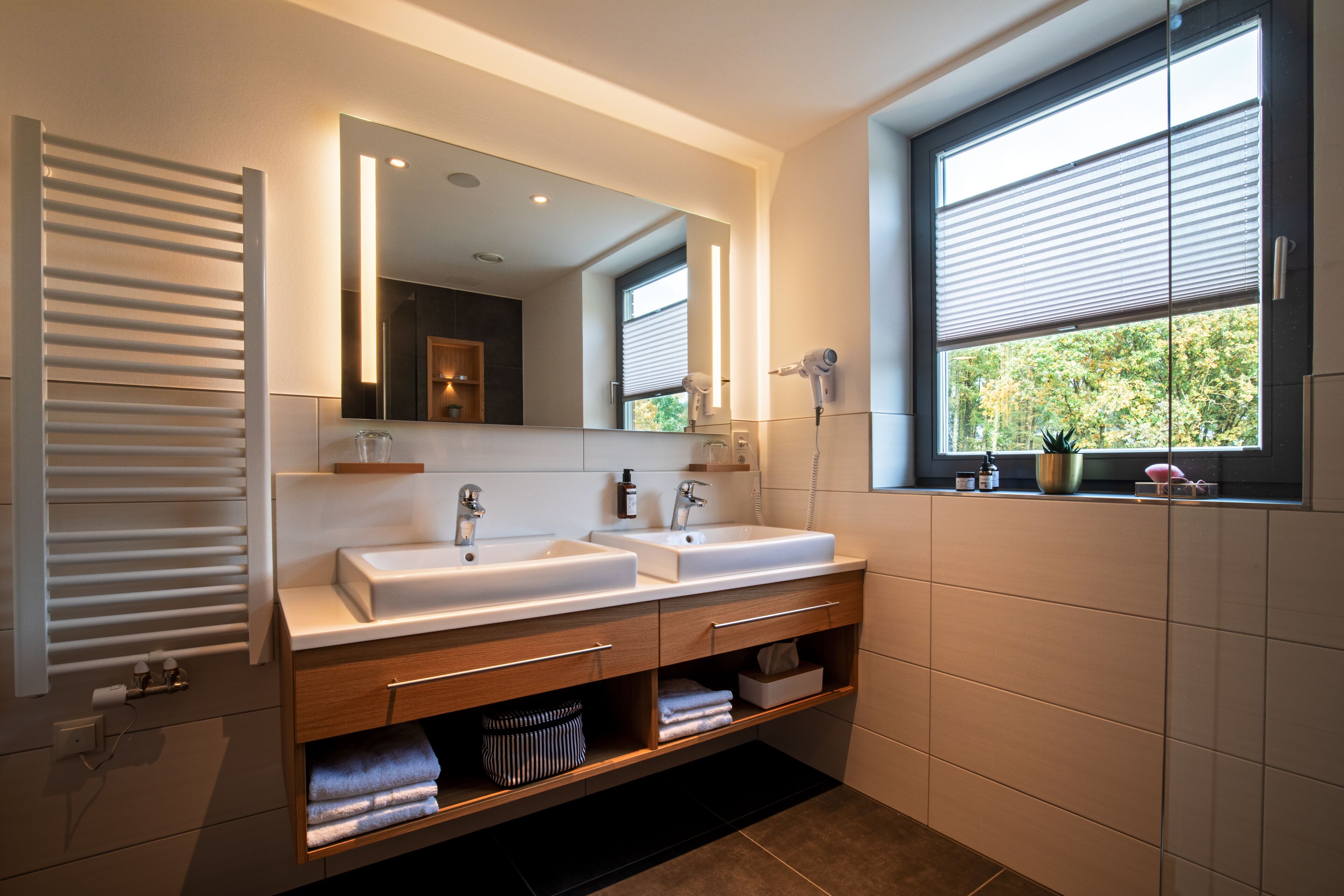 Un baño moderno con dos lavamanos, un espejo grande y una ventana con persianas.