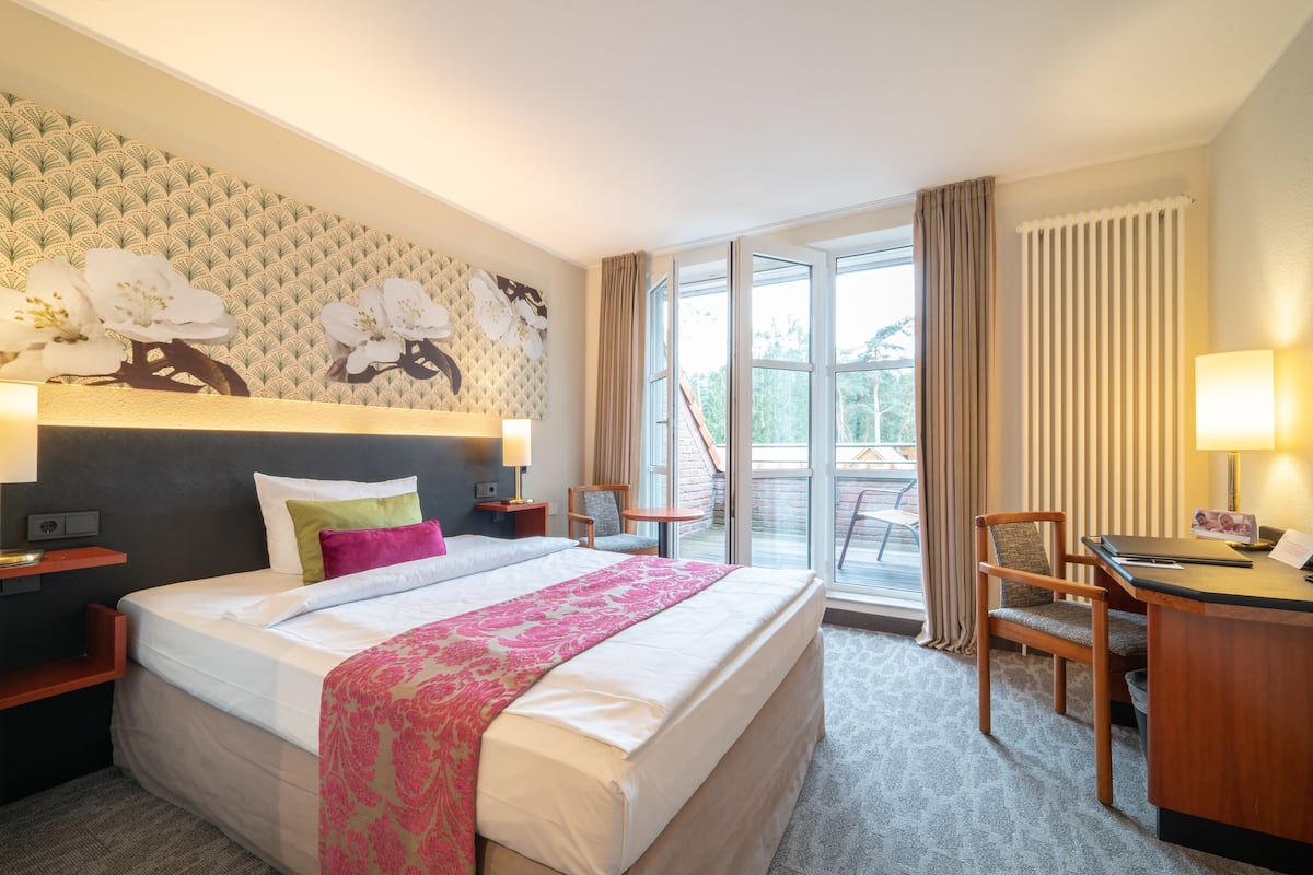 Ett hotellrum med en stor säng, ett skrivbord, en stol, ett fönster och utsikt över omgivningarna.