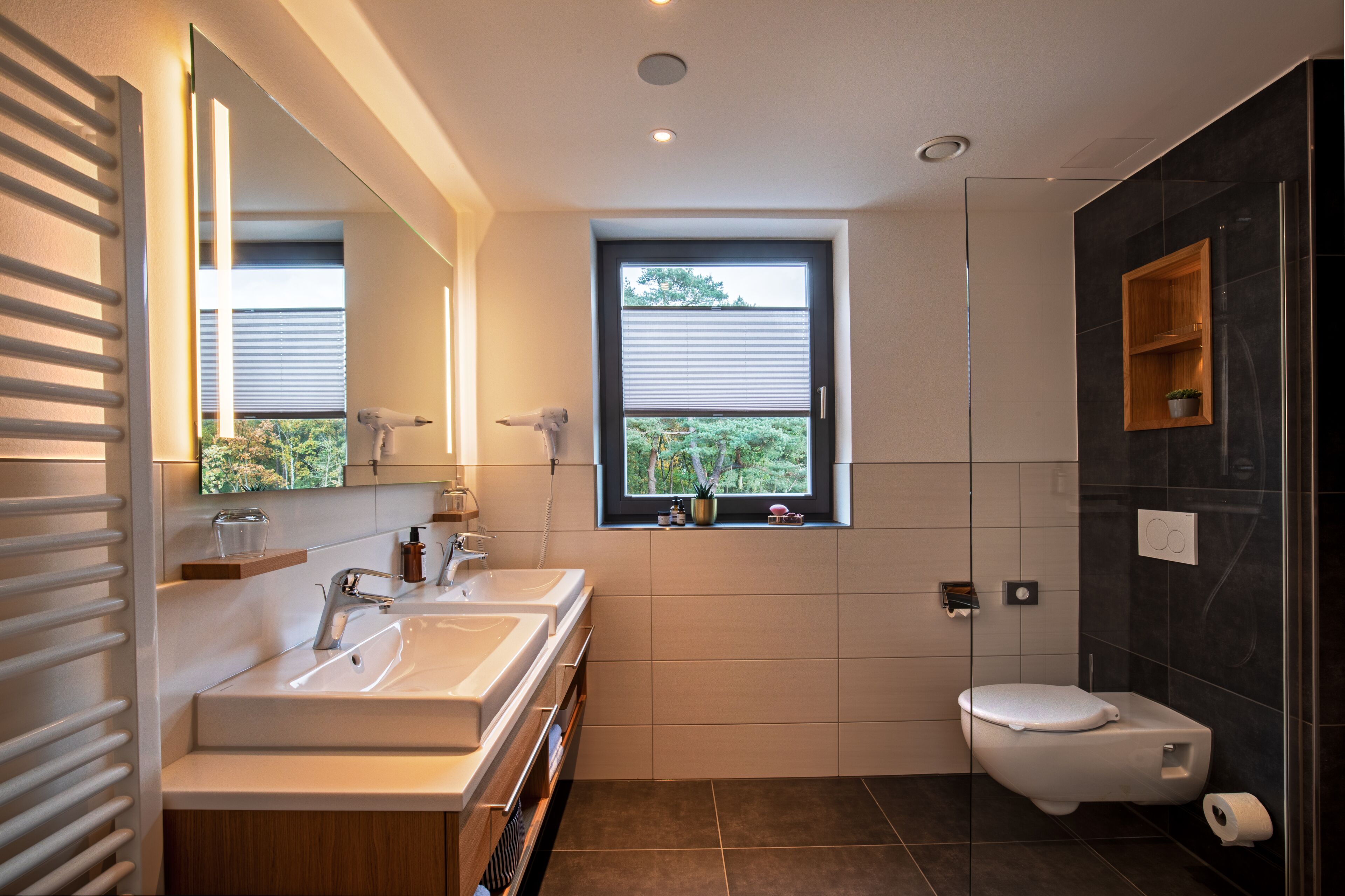 A modern bathroom with dual sinks, a toilet, and a window.