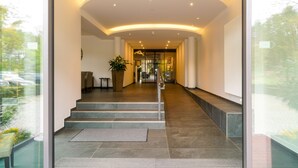 A modern hotel lobby with a curved ceiling, a staircase leading to the upper floor, and a large potted plant. - Heidegrund (Garrel)