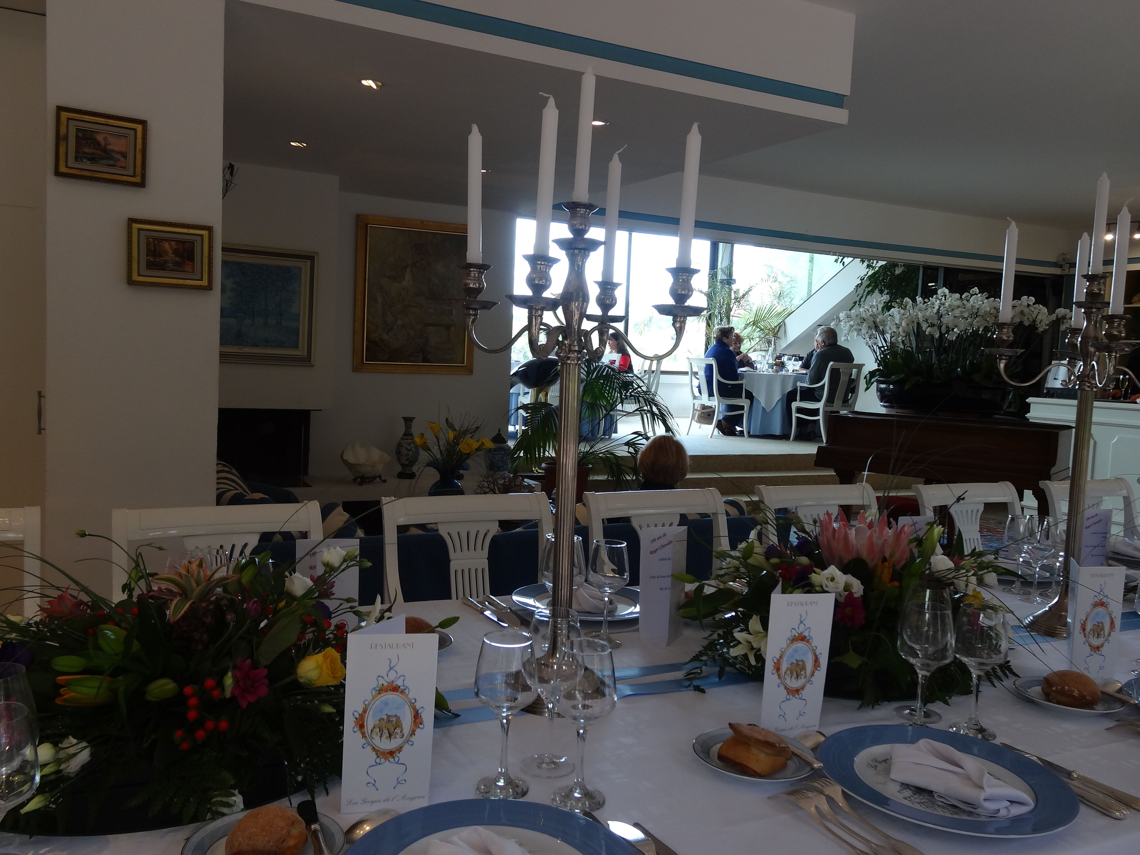 A formal dining area with tables set for a meal, featuring white tablecloths, blue plates, and candle holders.
