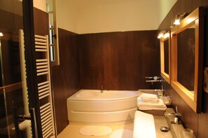 Un baño moderno con una bañera grande, cabina de ducha de vidrio y tocador de madera con espejo.