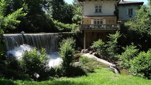 Un edificio de estilo arquitectónico tradicional, una cascada al frente y abundante vegetación alrededor.