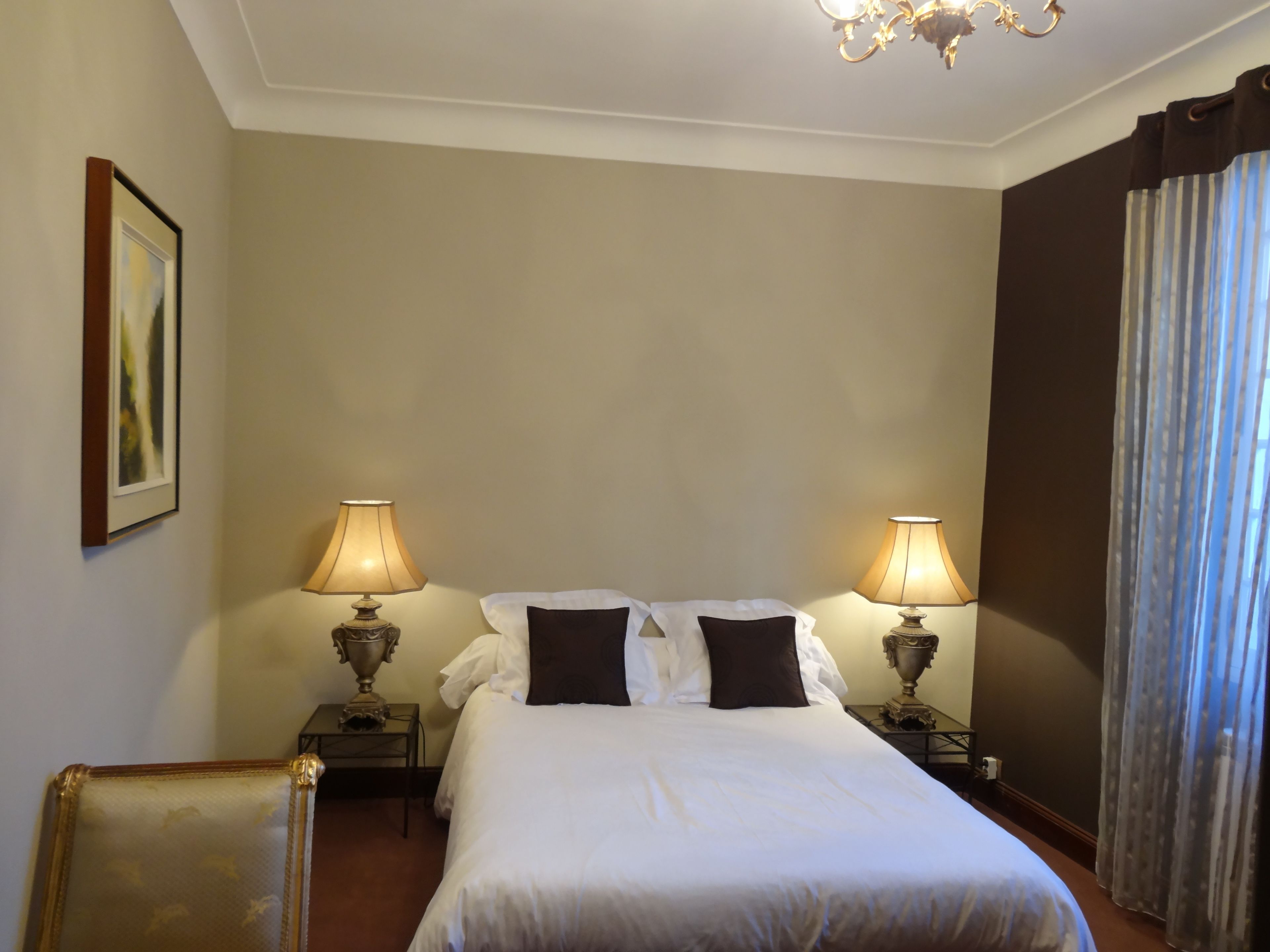 Habitación de hotel con una cama grande, dos lámparas de noche, un cuadro enmarcado en la pared y un candelabro.