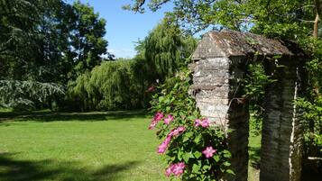 Een stenen gebouw overwoekerd met klimplanten en bloemen, omgeven door een gazon en bomen.