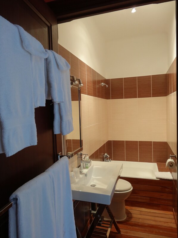 A bathroom with a sink, toilet, and shower. There are towels hanging on a rack.