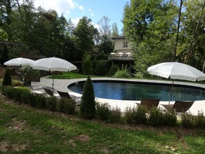 Una piscina con sombrillas blancas, rodeada de vegetación y una casa al fondo.