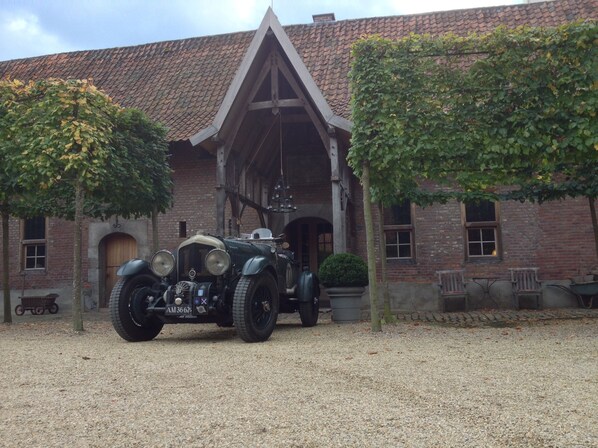 A vintage car parked in front of a brick building with a tiled roof and a wooden structure.