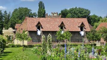 Un bâtiment traditionnel en pierre, doté d’un toit en tuiles, entouré d’un jardin bien entretenu où poussent différentes espèces de plantes à fleurs.