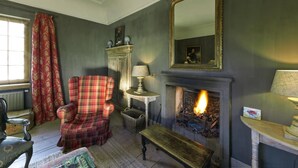 A traditional living room with a fireplace, plaid armchair, and a large mirror.