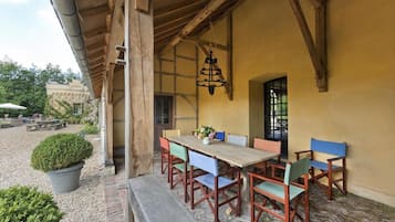 Un espace de restauration en plein air avec une table et des chaises en bois, un luminaire suspendu et une vue sur le jardin et les bâtiments environnants.