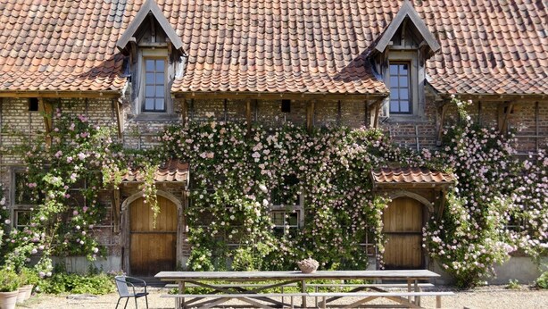 A rustic building with a tiled roof, wooden doors, and a garden with climbing roses.