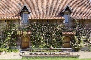 A rustic building with a tiled roof, wooden doors, and a garden with climbing roses.