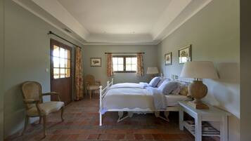 Une chambre à coucher avec un lit double, deux tables de chevet, une chaise, une fenêtre avec des rideaux et une porte.