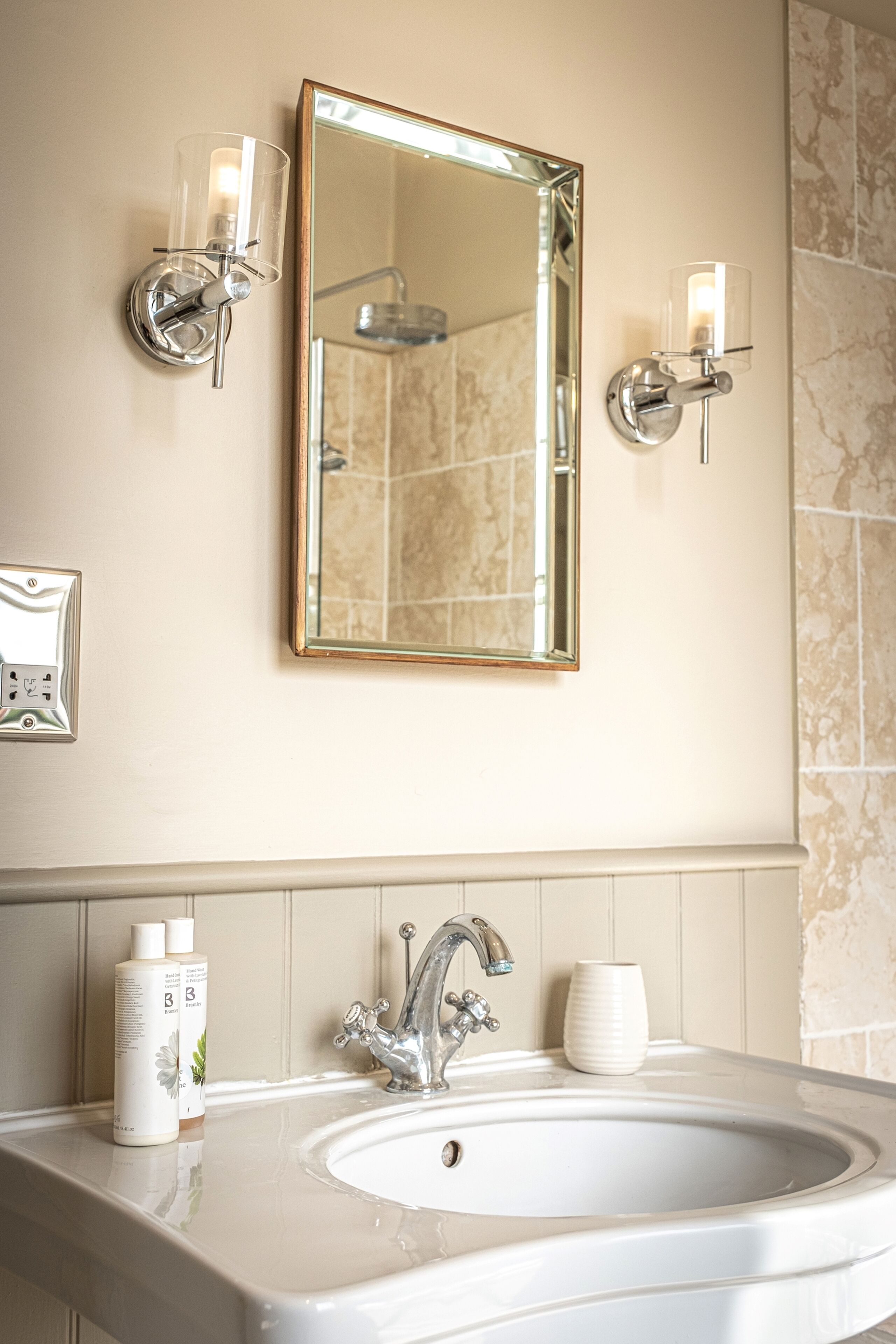 A bathroom with a large mirror, two wall-mounted lights, a sink, and toiletries.