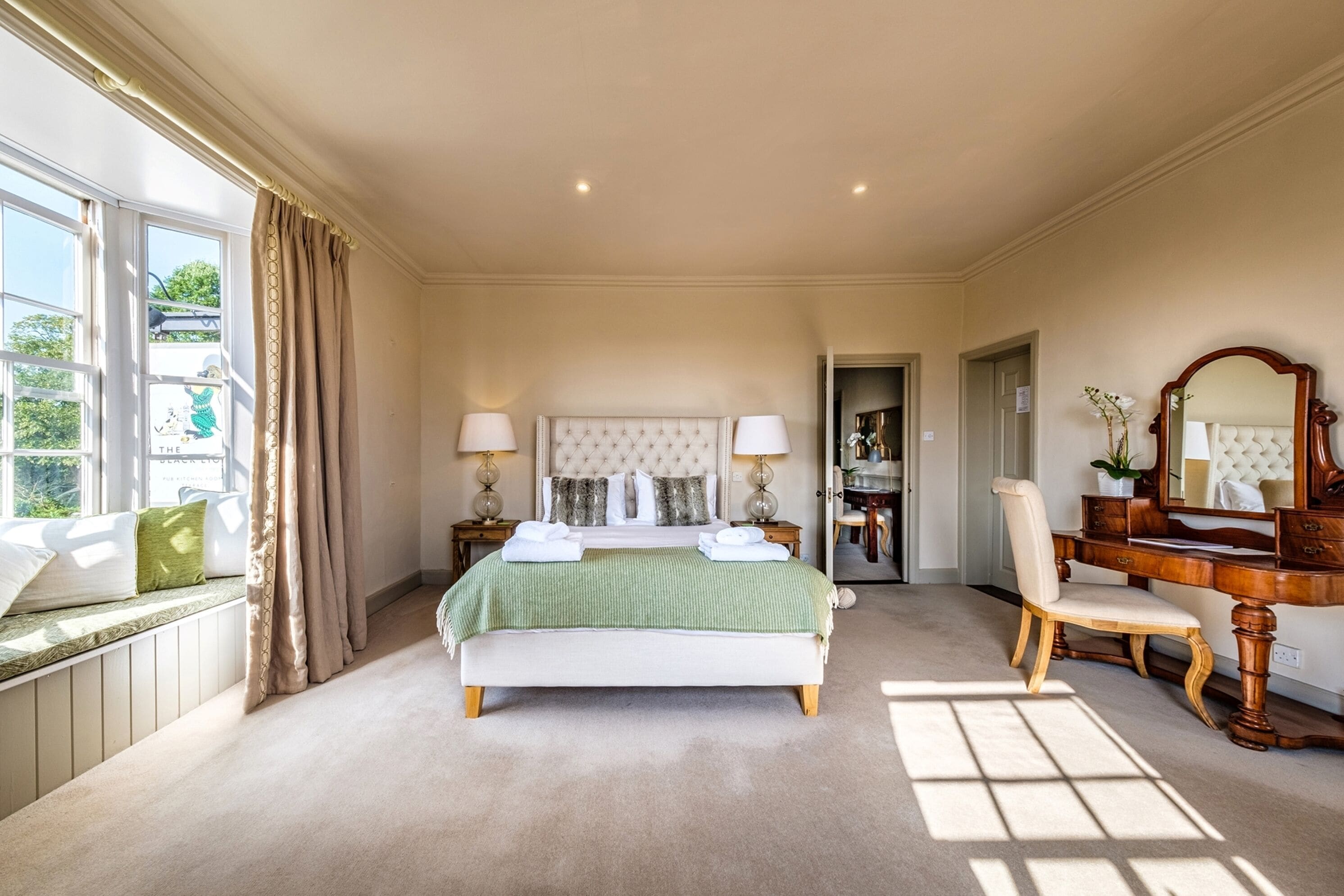 A bedroom with a large bed, a vanity with a mirror, and a window with curtains.