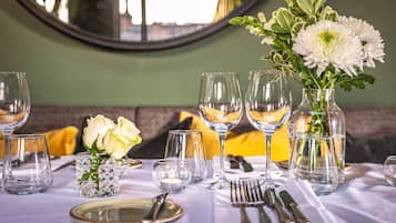 Une table à manger dressée avec de la vaisselle transparente, des assiettes et des couverts, agrémentée d’un vase de fleurs blanches et d’une bougie.