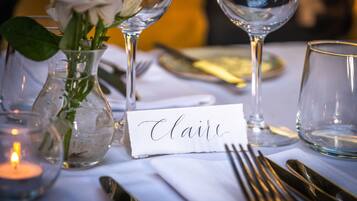 A table set with a name card, a glass vase with a white rose, and a lit candle.