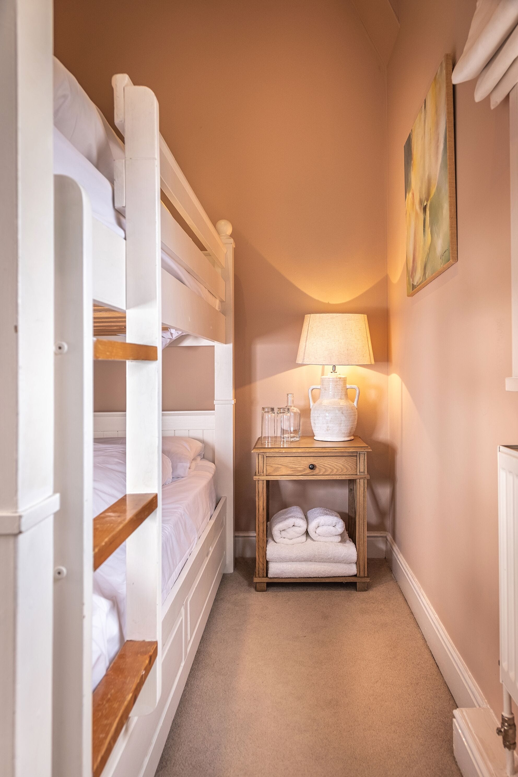 A narrow hallway with bunk beds, a bedside table with a lamp, and a radiator.