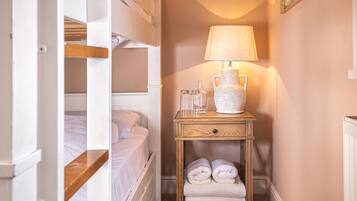 A narrow hallway with bunk beds, a bedside table with a lamp, and a radiator.