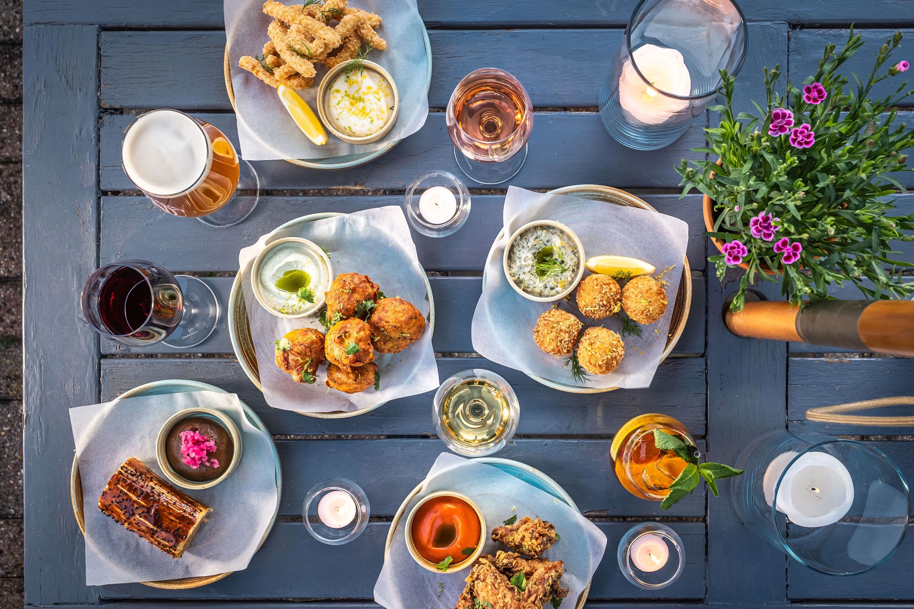 A table set with various dishes, drinks, and a potted plant.