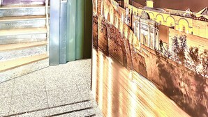 A reception area with a staircase leading to the 1st floor, a reception desk labeled "RECEPCIÓN 1ª PLANTA", and a mural depicting a historical building. - Arriadh (Córdoba)