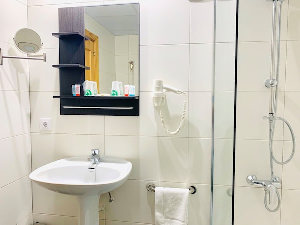 A bathroom with a white sink, a mirror, a shower, and a shelf with toiletries. - Arriadh (Córdoba)