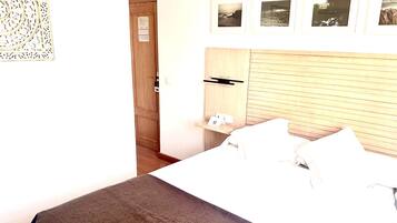 Habitación de hotel con cama, cabecera de madera, estante pequeño con un teléfono y una tarjeta, y puerta con un calendario.